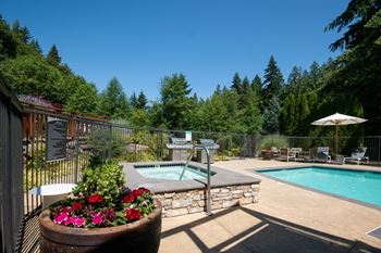 A pool surrounded by a fence and trees with a hot tub in the middle.